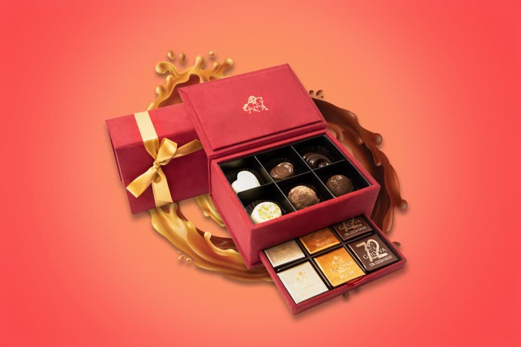 Red Godiva gift box open to show assorted chocolates, on a coral background