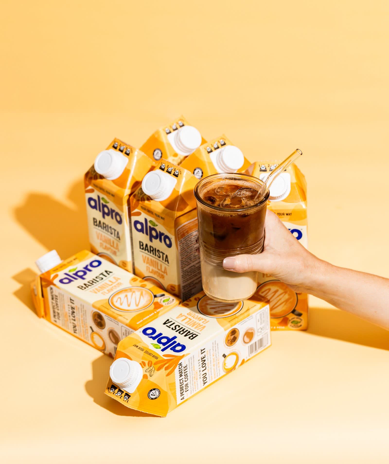 Stacked Alpro cartons with a poured iced drink, showing packaging under studio lighting