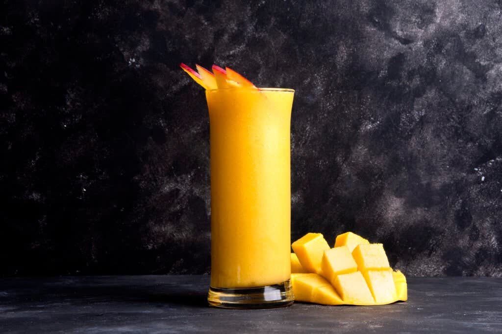 Mango smoothie in a tall glass with fanned mango slices and a cubed mango cheek