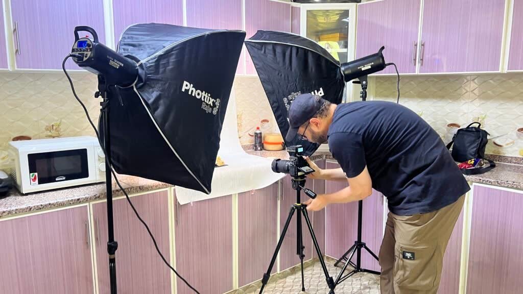 Photographer shooting a dish on a white paper sweep between two softboxes in a kitchen