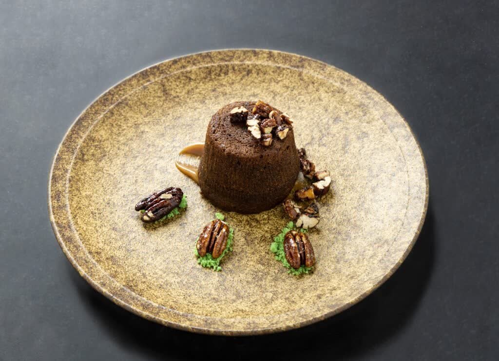 Plated chocolate dessert with pecans on a textured ceramic plate, photographed on a dark surface