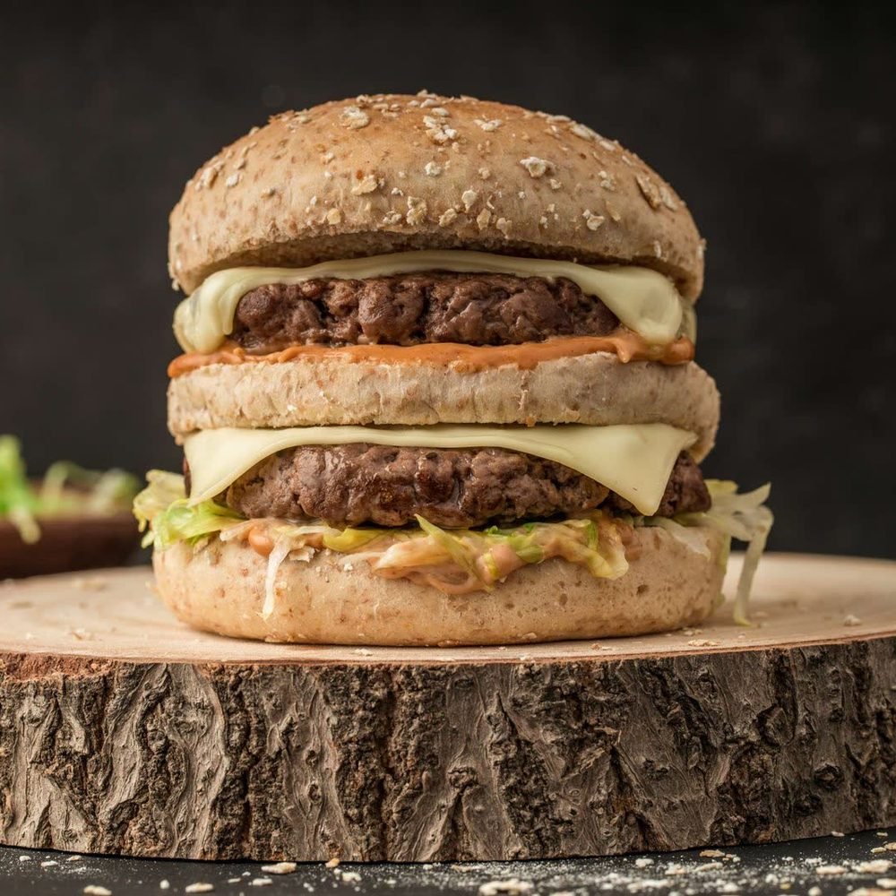 Double cheeseburger on a wooden slice, cropped to a square with the whole burger in frame