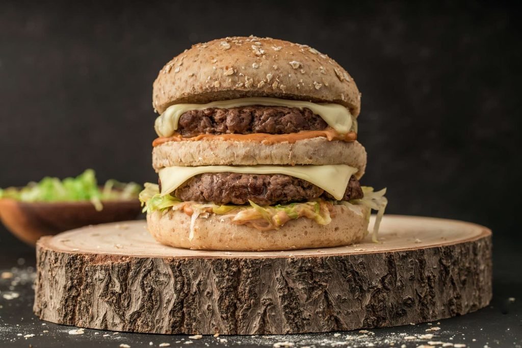 Double cheeseburger shot side-on and centred on a wooden slice against a dark backdrop