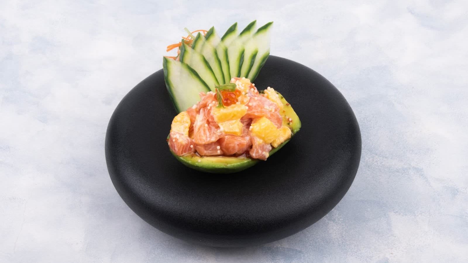 Salmon and mango poke in a halved avocado, centred on a black dish, shot landscape