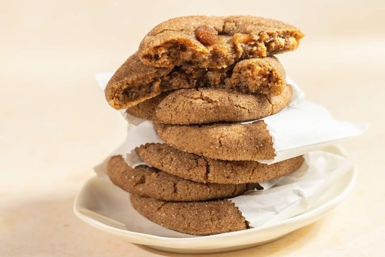 Stack of sugar-dusted cookies, the top two broken open, on a cream plate with parchment
